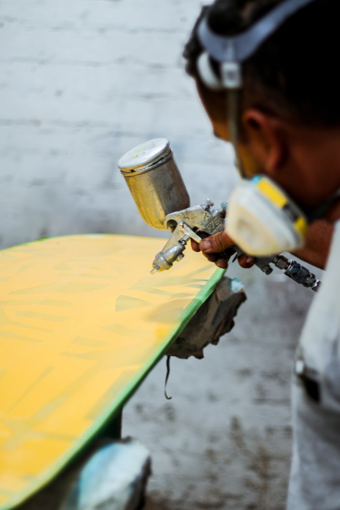 A worker in protective gear spray paints a wooden object indoors, showcasing craftsmanship.